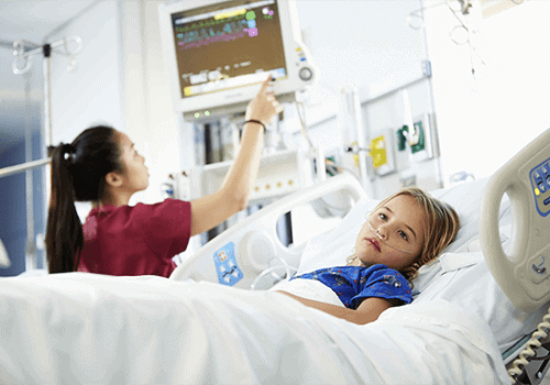 小女孩躺在医院重症监护室病床上的照片。当护士在医疗机器上监视她的状态时，她脸上露出不悦的表情。