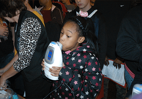 黑人女孩对着呼吸测量工具吹气以检测哮喘的照片