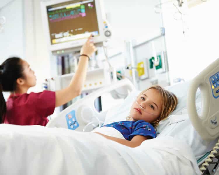 小女孩躺在医院重症监护室病床上的照片。当护士在医疗机器上监视她的状态时，她脸上露出不悦的表情。