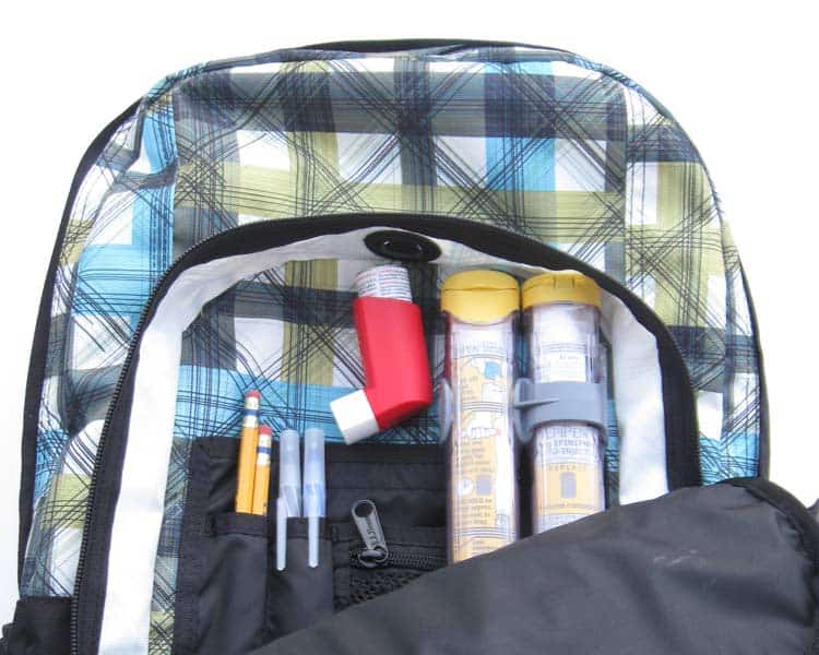 格子背包有一个打开的盖子两个肾上腺素自动注射器，哮喘吸入器，还有钢笔