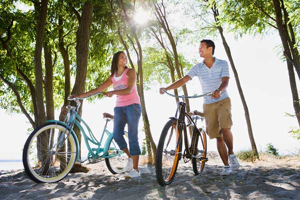 一对夫妇在公园里骑自行车。他们在树下，远离夏天的阳光。