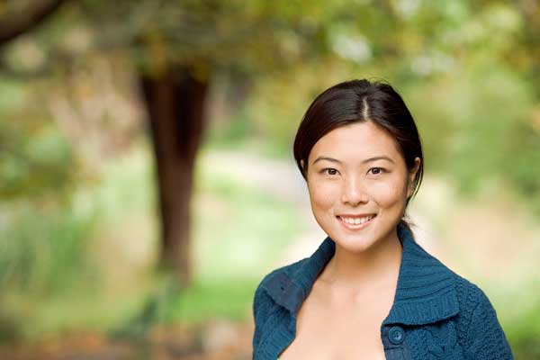 年轻的亚洲女子面对镜头微笑。在一个美好的春日里，她在公园里。