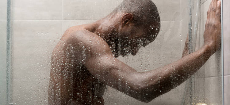 黑人男子快速淋浴的照片。水源性荨麻疹引起的荨麻疹使他的头低垂着