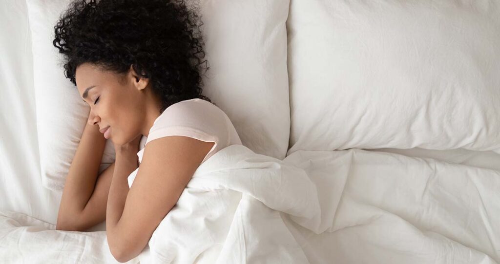 african american woman sleeping in comfortable bed lying on soft pillow orthopedic mattress, peaceful young black lady resting covered with blanket on white sheets in bedroom, top view