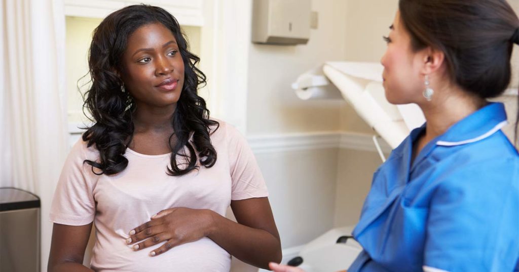 Pregnant Black woman getting advice on asthma medications from her doctor.