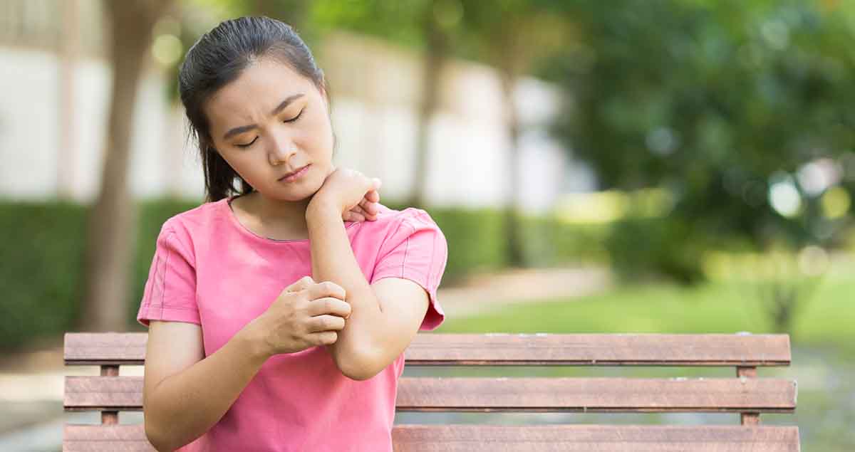 asian Woman scratching her arm while outside sitting on a park bench
